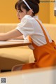 A woman sitting at a table wearing an orange apron.