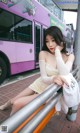 A woman sitting on a railing in front of a bus.