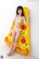 A woman in a bikini sitting on an inflatable pizza slice.