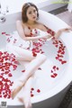 A woman sitting in a bathtub filled with rose petals.