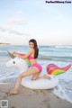 A woman in a pink bikini sitting on an inflatable unicorn on the beach.