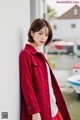 a woman in a red coat leaning against a wall