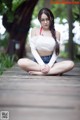 A woman sitting on a wooden boardwalk in a white top and blue shorts.