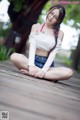 A woman sitting on a wooden deck in a white top and blue shorts.