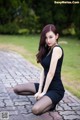 A woman in a black dress sitting on a brick walkway.